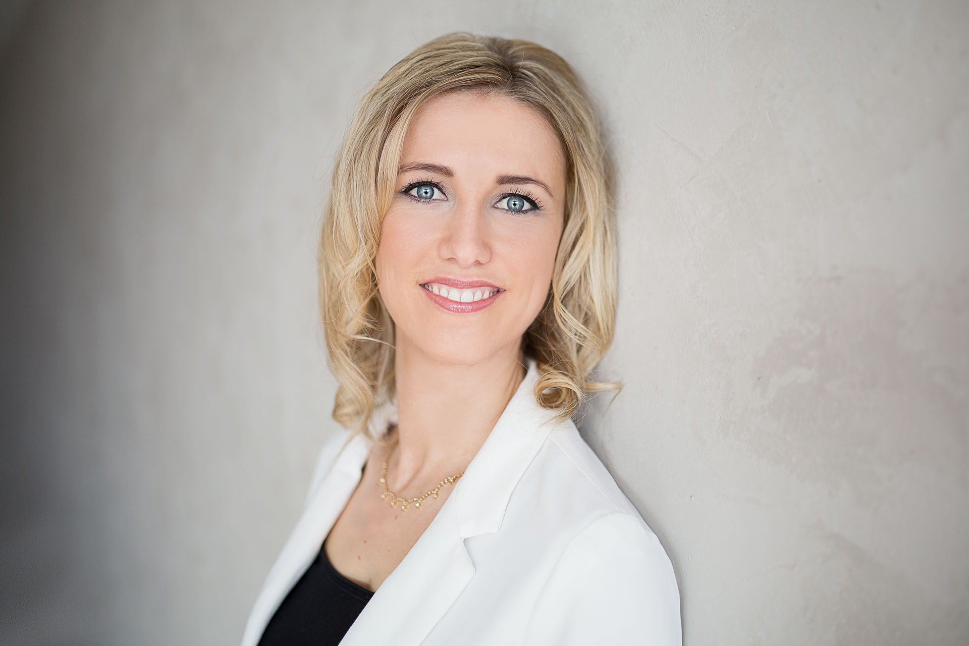 Frau in weißem Blazer, an die wand lehnend