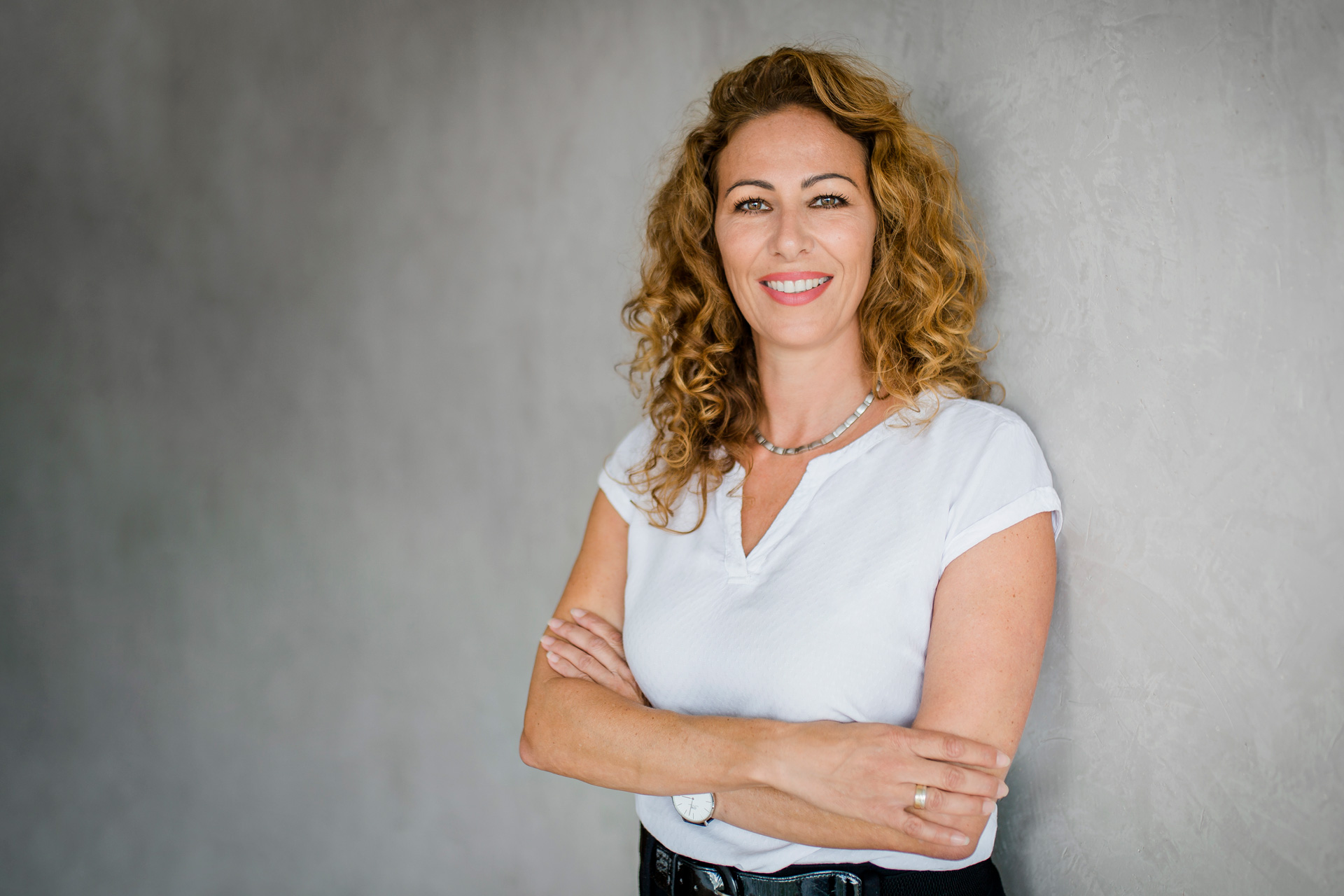 Frau mit lockigem Haar und verschränkten Armen.